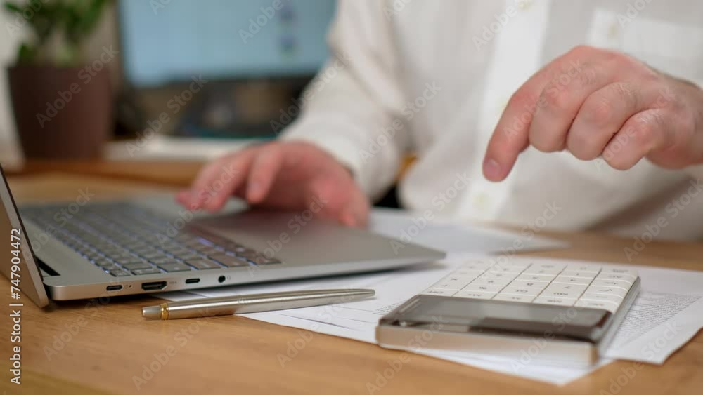 Man Working in Office, Using Laptop Computer and Calculator Placed on Desk, close up. Male entrepreneur working at notebook with online trading market finance digital data Man Working in Office, Using Laptop Computer and Calculator Placed on Desk, close up. Male entrepreneur working at notebook with online trading market finance digital data
