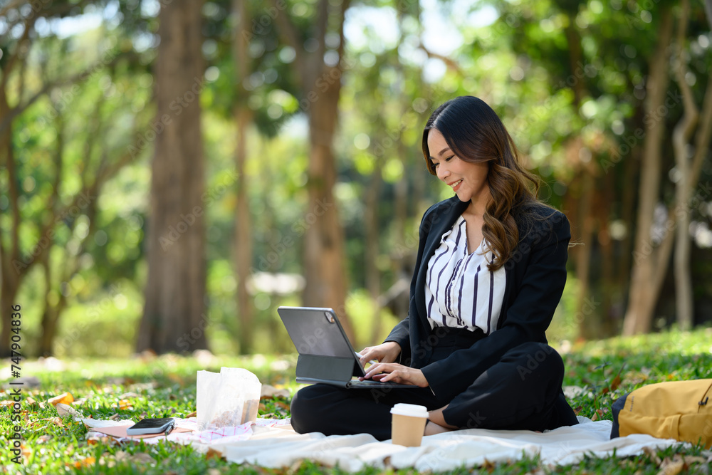 Charming businesswoman working on digital tablet sitting on grass in the park Charming businesswoman working on digital tablet sitting on grass in the park