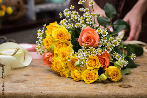 Bouquet of roses and daisies on the table the store close-up.Florist in an apron tying a ribbon on a bouquet.The process of creating a bouquet.Education and courses in floristry.