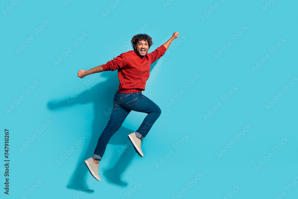 Full length photo of young hispanic superman hero flying and jumping raised fist up motivation banner isolated on blue color background