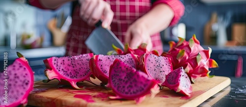 A person is seen cutting and peeling dragon fruit halves on a cutting board in a home kitchen. The fruit will be used to make juice.