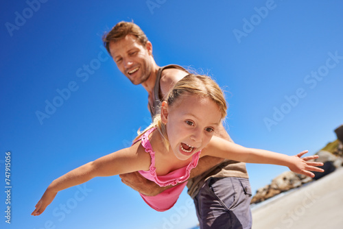 Happy dad, beach and flying with child for fun summer, holiday or outdoor weekend together in nature. Father, little girl or playing with daughter for freedom in sun by the ocean coast with blue sky © MV/peopleimages.com