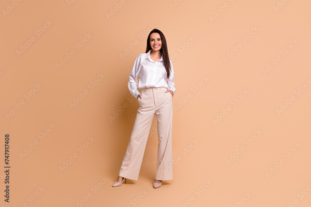 Full size portrait of lovely positive lady put hands pockets posing empty space isolated on beige color background Full size portrait of lovely positive lady put hands pockets posing empty space isolated on beige color background