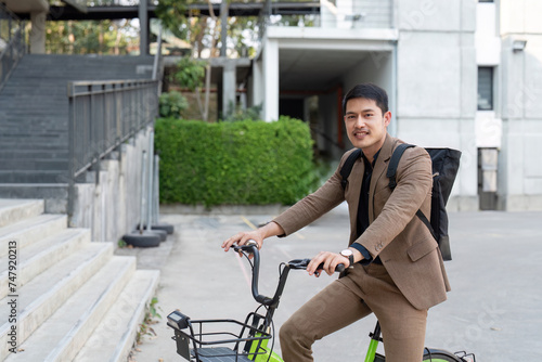 Fototapeta Naklejka Na Ścianę i Meble -  Asian businessman in a suit is riding a bicycle on the city streets for his morning commute to work. Eco transportation concept, sustainable lifestyle concept