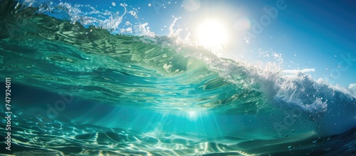 The sun shines brightly over the clear ocean waves during summertime, reflecting its rays on the surface and under the blue waters, creating a stunning sight.