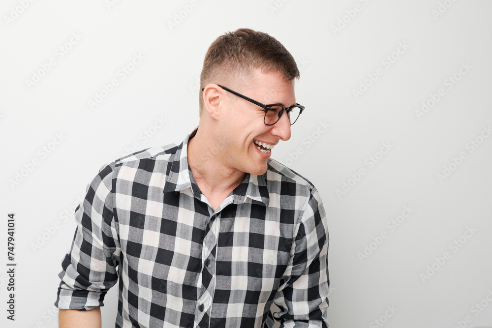 Cheerful young man in glasses and plaid shirt laughing against a white background. Cheerful young man in glasses and plaid shirt laughing against a white background.