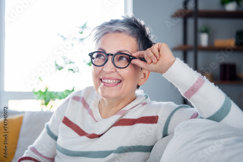 Photo of thoughtful dreamy woman dressed striped sweater hand arm eyewear sitting couch indoors house home room