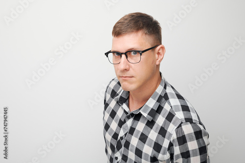 Portrait of skeptical young man in glasses and checkered shirt, looks at camera on white background
