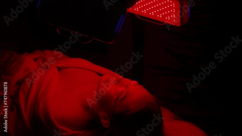 Close-up face of female client lying during non-invasive type of phototherapy. Closeup of woman patient in protective goggles undergoes blue LED light therapy for skin rejuvenation at aesthetic clinic photo