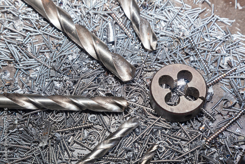 Drill bits for drilling steel lie on steel shavings close-up. Thread cutting die