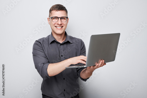 Professional man in glasses using laptop against a gray background with a focused expression.