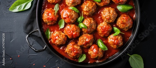 A perspective shot from above of a pan filled with Swedish meatballs swimming in rich tomato sauce on a black background, highlighting the appetizing and savory dish.