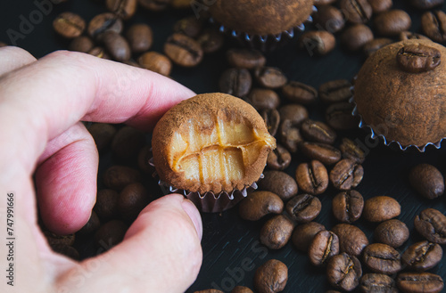 Um brigadeiro de café delicadamente na mão disposto em uma base de forminha marrom, adornado com grãos de café, em meio a uma decoração. A coffee brigadeiro delicately arranged in a brown base.