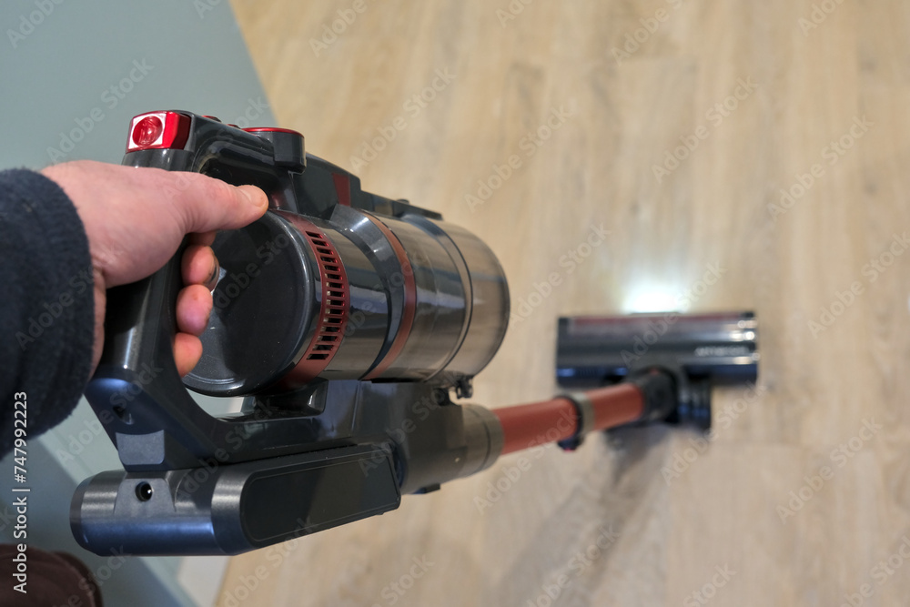 Top view of a hand holding a stick vacuum cleaner. The body is clear and the head is blurred.