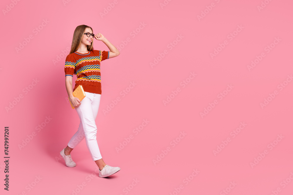 Full length profile portrait of positive smart girl hand touch eyewear hold book walk empty space isolated on pink color background