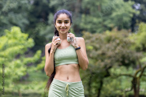 Active indian woman in green tracksuit with headphones preparing for park fitness