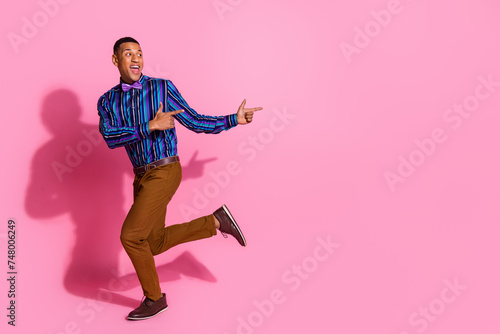 Full length photo of excited funky guy dressed striped shirt pointing two fingers empty space isolated pink color background