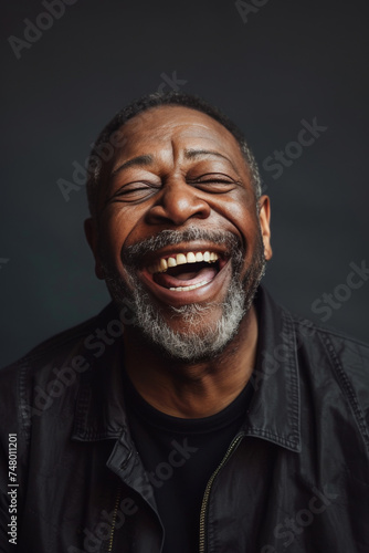 Senior man with beard laughing heartily against dark backdrop