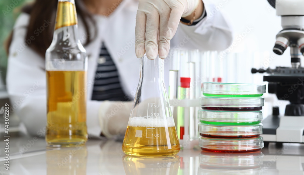 Close-up of assistant hands pouring yellow liquid into flask. Professional scientist making mixture of fluid for experiment. Chemical researching and quality test concept Close-up of assistant hands pouring yellow liquid into flask. Professional scientist making mixture of fluid for experiment. Chemical researching and quality test concept