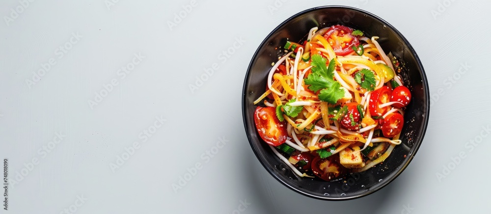 A black bowl is filled with a savory mix of noodles, assorted vegetables, and Thai papaya salad seen from above on a white surface. The dish appears spicy and inviting. A black bowl is filled with a savory mix of noodles, assorted vegetables, and Thai papaya salad seen from above on a white surface. The dish appears spicy and inviting.