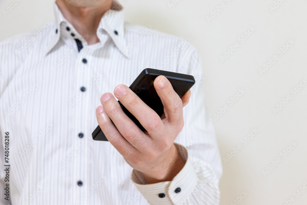 片手にスマートフォンを持つ白いシャツ姿の男性 片手にスマートフォンを持つ白いシャツ姿の男性