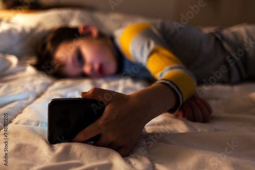 Photo of small boy using cell phone in the dark. Cute boy watching cartoons on smart phone at night. Copy space.