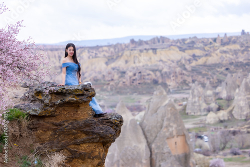 Beautiful woman in blue dress on Turkey rocks mountain.Cheerful woman relax outdoor with beautiful sky and pink flowers in holiday vacation.Woman tourist enjoy amazing mountain view.Travel and freedom