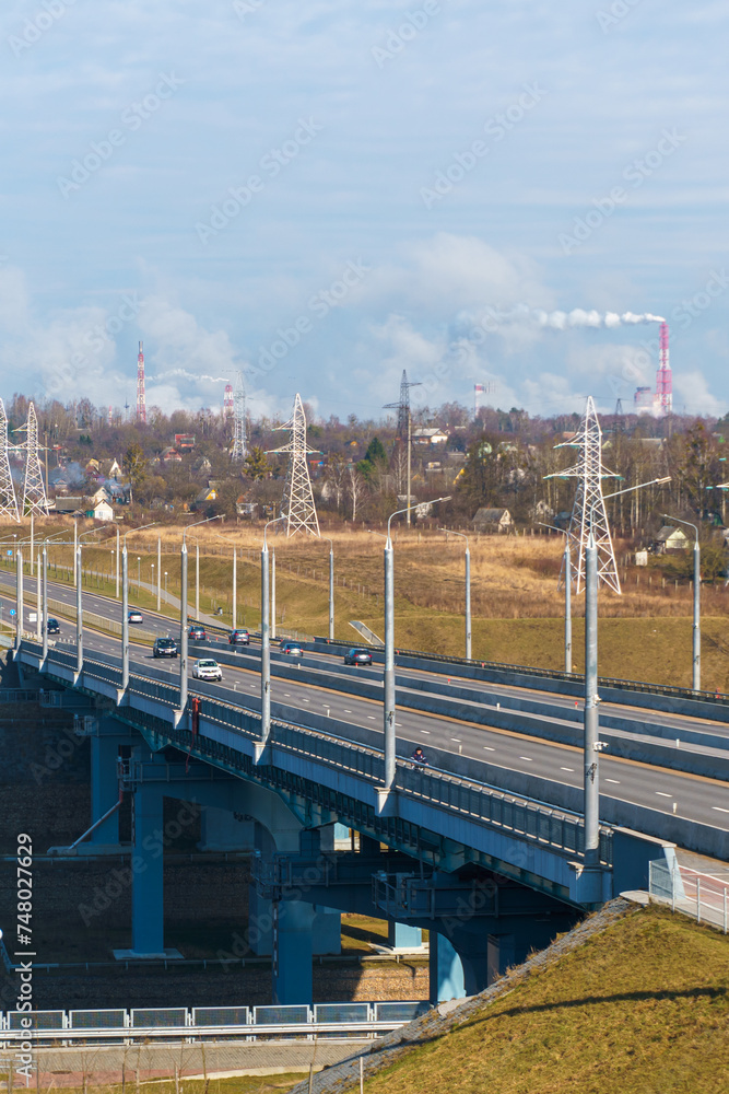 A new modern automobile bridge over the river on the background of the blue sky. A sturdy reinforced concrete bridge, thick concrete arches and metal floors. A new modern automobile bridge over the river on the background of the blue sky. A sturdy reinforced concrete bridge, thick concrete arches and metal floors.