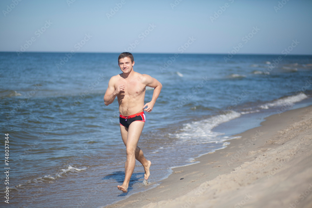 A man in swimming trunks runs along the sea along the shore. Jogging along the ocean. A man with a naked torso and an athletic build