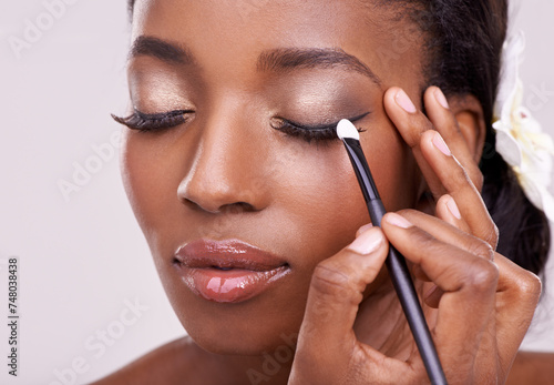 Black woman, face and brush for eyeshadow with beauty, makeup and lashes on grey background. Skin glow, hands and apply cosmetic product with tools for cosmetology, shimmer or glitter with shine photo