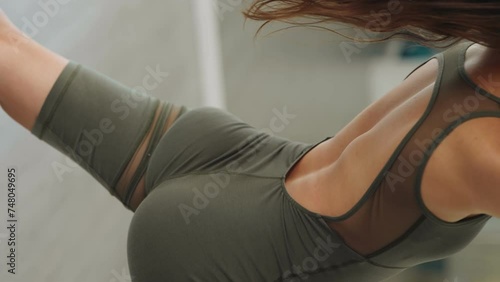 Captivating vertical view of a fit woman in athletic wear engaging in a lower back and glute stretch during a focused studio workout session. photo