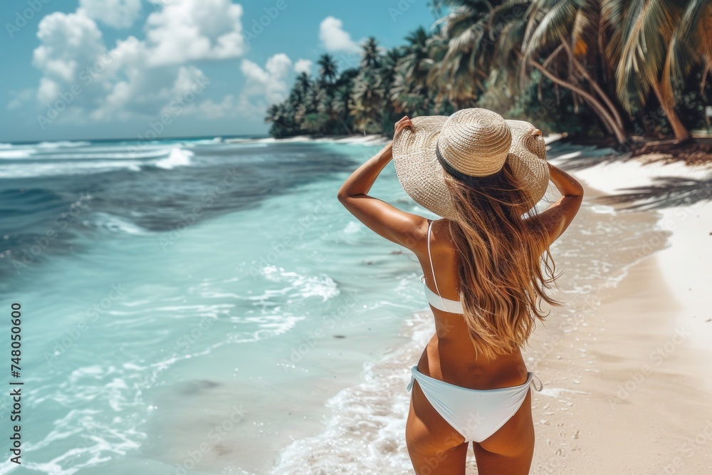 Naklejka premium Back view of a young woman wearing straw hat on a beautiful tropical beach