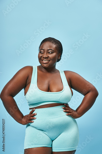 plus size african american woman in stylish active wear looking back and posing with hands on hips