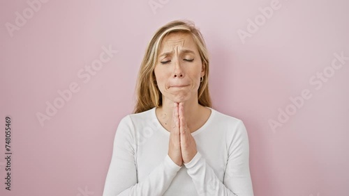 Confident young blonde woman praying, hands together asking for forgiveness, incredibly beautiful over isolated pink background, spiritual power smiling vividly photo