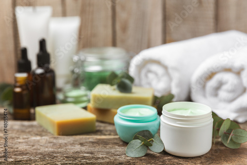 Beautiful spa composition on a wooden background with eucalyptus leaves. Beauty and fashion spa concept with body cream, scrub, mask, essential oil and sea salt.Cosmetic product. Copy space.