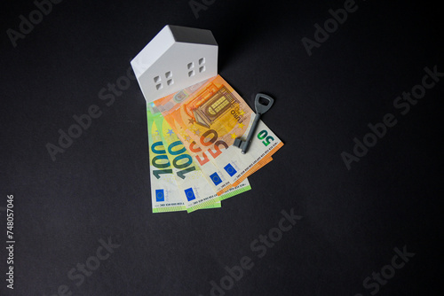 wooden house with euro money and key on black background. concept, people tied themselves to the bank for a mortgage