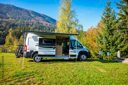 Campervan or motorhome with bicycle rack parked in the nature countryside. Camper van or  motor home is camping in a meadow surrounded by forest and hills. Active family vacation in Slovenia.