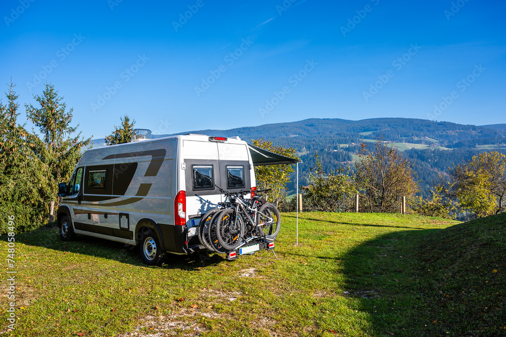 Campervan or motorhome with bicycle rack parked in the nature countryside. Camper van or motor home is camping in a meadow surrounded by forest and hills. Active family vacation in Slovenia. Campervan or motorhome with bicycle rack parked in the nature countryside. Camper van or motor home is camping in a meadow surrounded by forest and hills. Active family vacation in Slovenia.