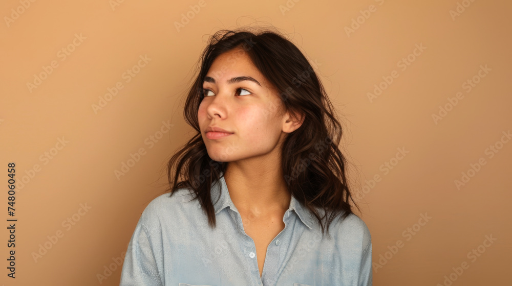 A young woman with shoulder-length hair gazes to the side against a neutral beige background, wearing a light blue shirt. A young woman with shoulder-length hair gazes to the side against a neutral beige background, wearing a light blue shirt.