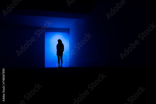 Fototapeta Naklejka Na Ścianę i Meble -  Une silhouette de femme bleu debout dans un décor architectural sombre et bleu