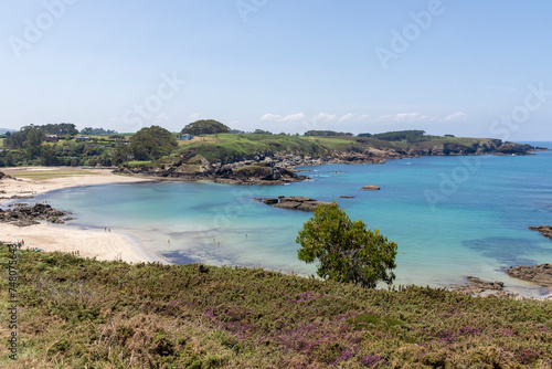 a serene beach scene with calm  turquoise waters  a sandy shore bordered by rocky outcrops and lush greenery under a clear sky. A few people are visible at a distance