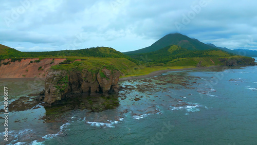 Top view of rocky coast with algae on shore. Clip. Landscape of rocks on coast with algae on background of mountains in cloudy weather. Diversity of flora of sea coast with rocky mountains