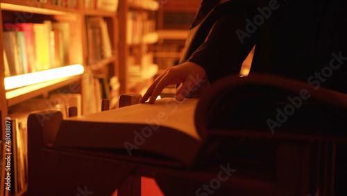 Close-up of mysterious man opening large book. Stock footage. Man opens book in dark library with flashing light. Secret society with mysterious books in night library