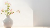 White vase with flowers on a countertop aganist a empty white wall bathed in sunlight.