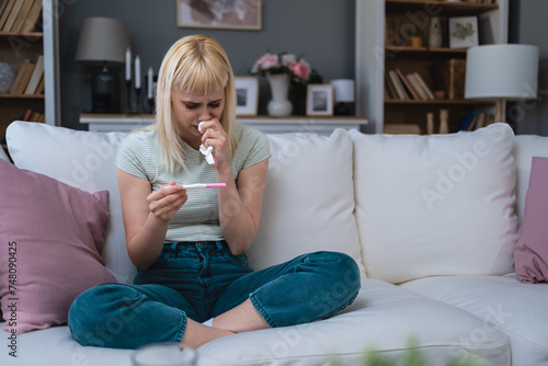 Bilde på lerret Single sad woman complaining holding a pregnancy test sitting on a couch in the living room at home, Stressed female, Positive or negative medical test pregnant or not