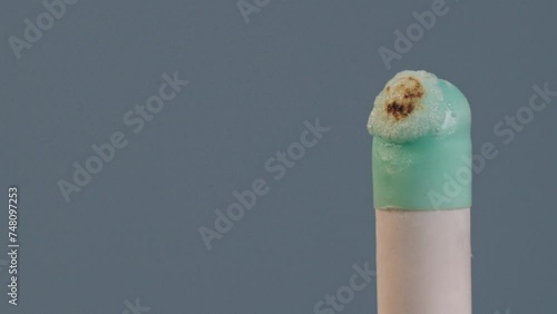 An ignited gelatin or agar pill of white and turquoise color, isolated on a grey background, burns, melts, foams, chars and turns into black lava mass under the influence of fire. The drugs and
