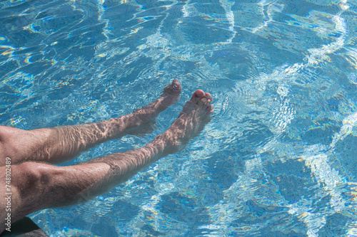 Man relaxing in swimming poll. Man legs in water.