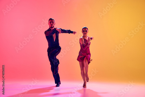 Fototapeta Naklejka Na Ścianę i Meble -  Male and female dancers performing a Latin dance in stylish clothes against gradient pink yellow background in neon light. Concept of dance class, hobby, art, dance school, talent