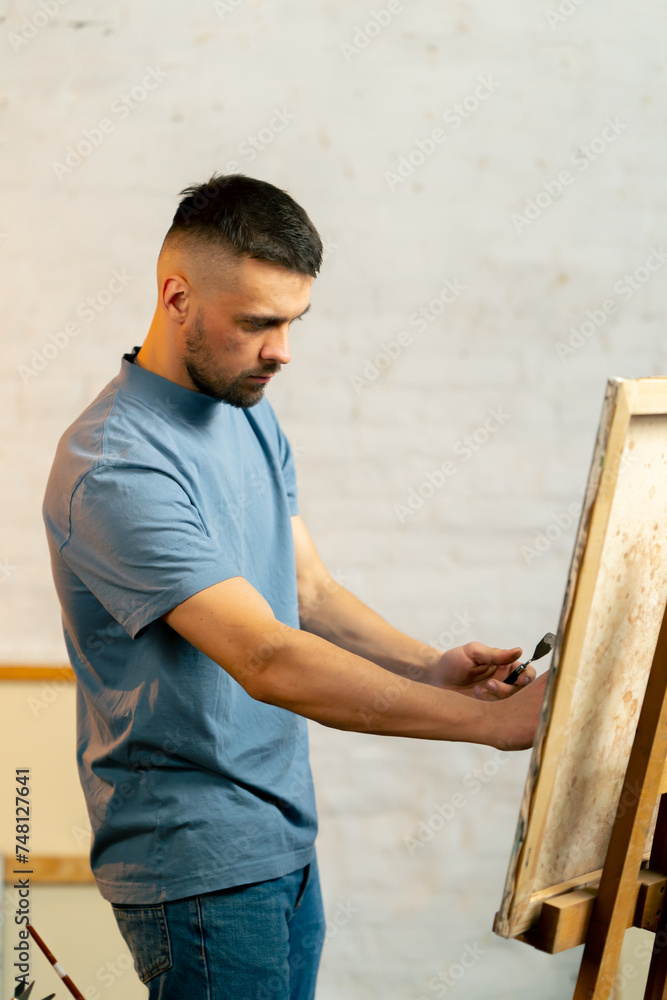 in an art workshop an artist in a blue T-shirt makes a wide stroke with a palette knife