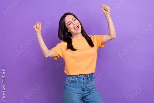 Photo of ecstatic satisfied woman with straight hairdo dressed orange t-shirt clenching fists win bet isolated on purple color background